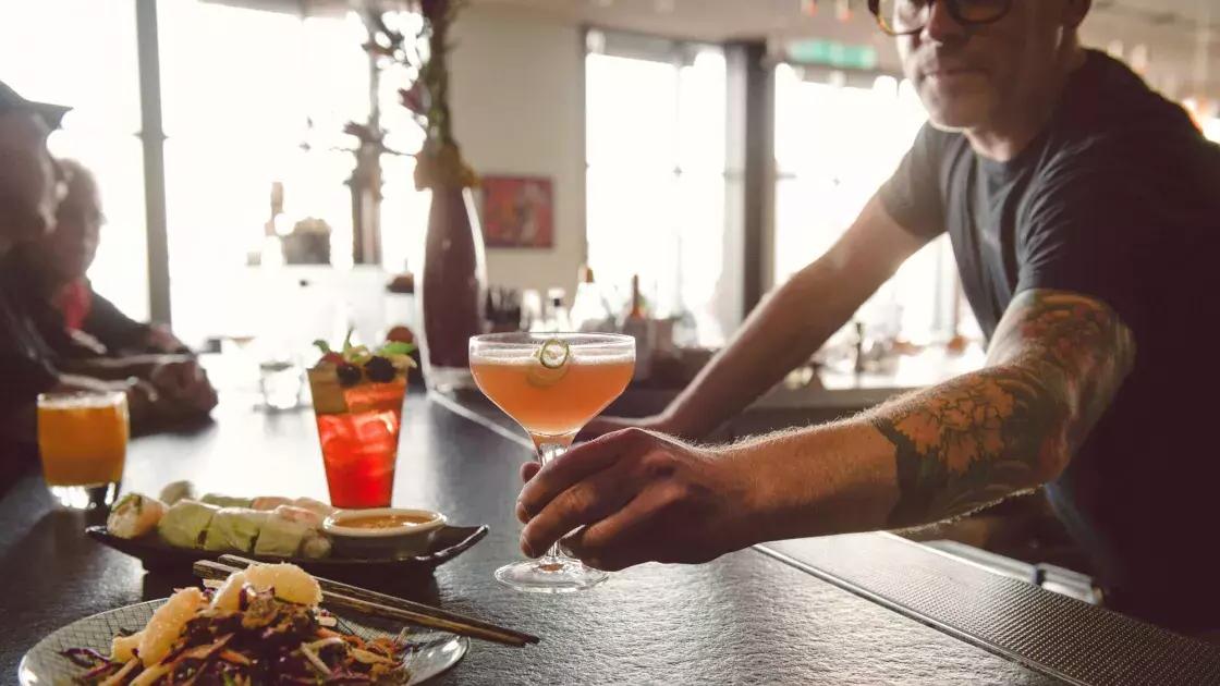 在贝博体彩app的一家酒吧里，酒保正在给顾客递鸡尾酒.